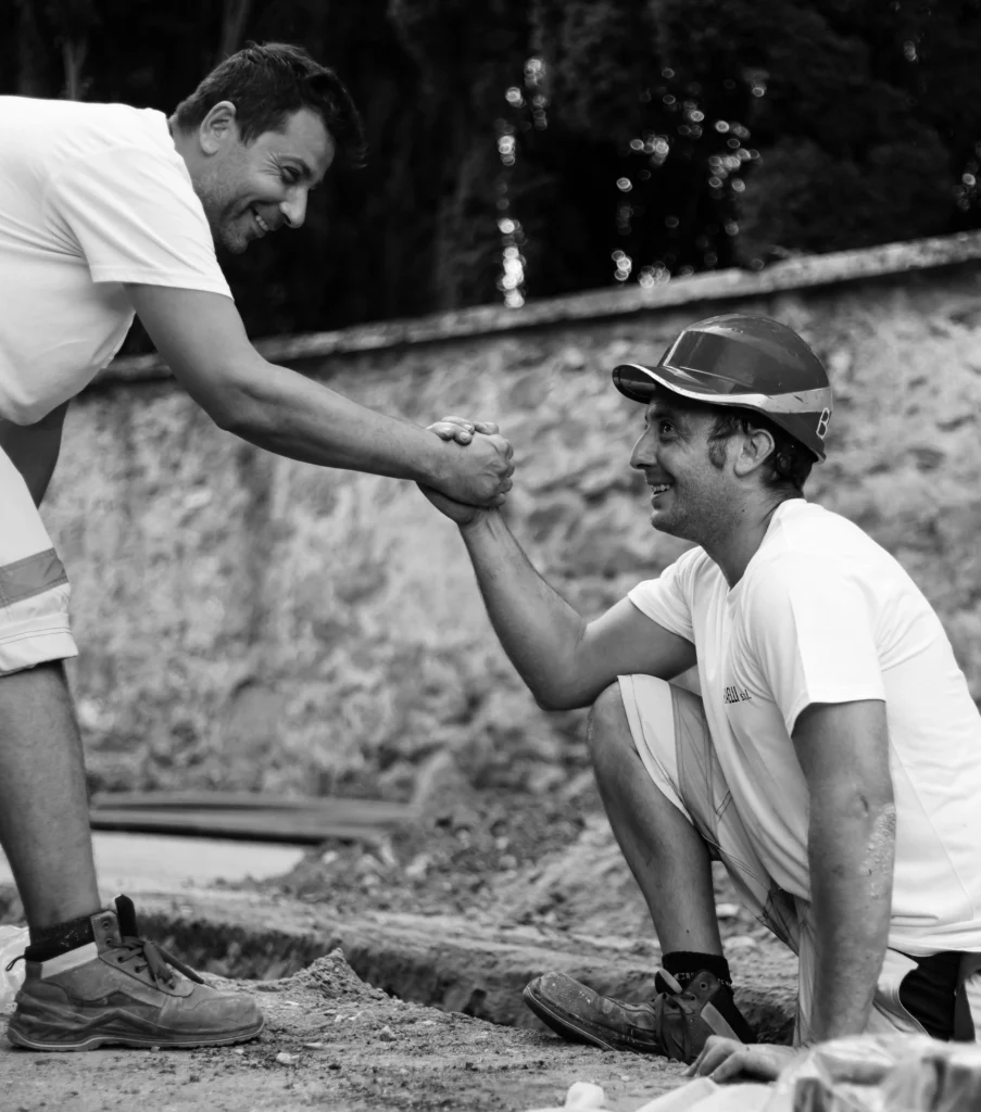 Un operaio aiuta un altro operaio a uscire da un fosso durante i lavori di rifacimento dell’asfalto